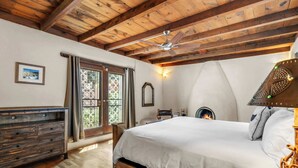 A bedroom with a wooden ceiling, a bed, a dresser, a fireplace, and a window with curtains.