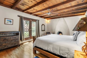Une chambre avec un plafond en bois, un lit, une commode, une cheminée et une fenêtre avec des rideaux.