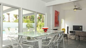 A modern living room with a glass dining table, clear chairs, a sofa, a TV, and a ceiling fan. - Contemporary Home with WiFi,Salt Water Pool, Jacuzzi-Your Own Retreat! (palm springs)