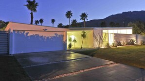 A modern house with a garage, a well-lit interior, and a view of palm trees and mountains in the background. - Contemporary Home with WiFi,Salt Water Pool, Jacuzzi-Your Own Retreat! (palm springs)