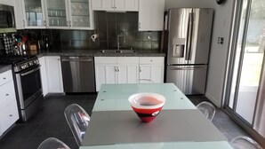 A modern kitchen with white cabinets, stainless steel appliances, and a glass dining table with a red bowl. - Contemporary Home with WiFi,Salt Water Pool, Jacuzzi-Your Own Retreat! (palm springs)