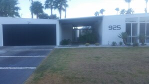A modern building with a large garage door, a number '925' on the facade, and a well-maintained lawn with cacti and shrubs. - Contemporary Home with WiFi,Salt Water Pool, Jacuzzi-Your Own Retreat! (palm springs)