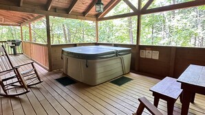 Une terrasse en bois avec un jacuzzi, des bancs en bois et des tables.