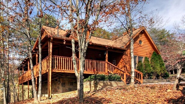 Une cabane en bois dotée d’un balcon, entourée d’arbres et de feuilles mortes.