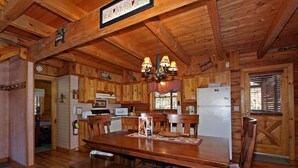 L’intérieur d’un chalet en bois comprend une table à manger, des chaises, un lustre et un réfrigérateur.
