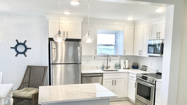 A modern kitchen with white cabinetry, stainless steel appliances, a central island with stools, and pendant lighting. - Beachfront Dream Cottage Sleeps 11 Beautiful PETS OK (Ocean City)