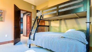 Une chambre avec un lit superposé, une échelle, une porte et une couvre-lit à motifs.
