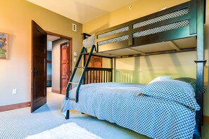 Ein Mehrbettzimmer mit einer Klapptreppe, einer Tür und einer Betttdecke mit Muster.