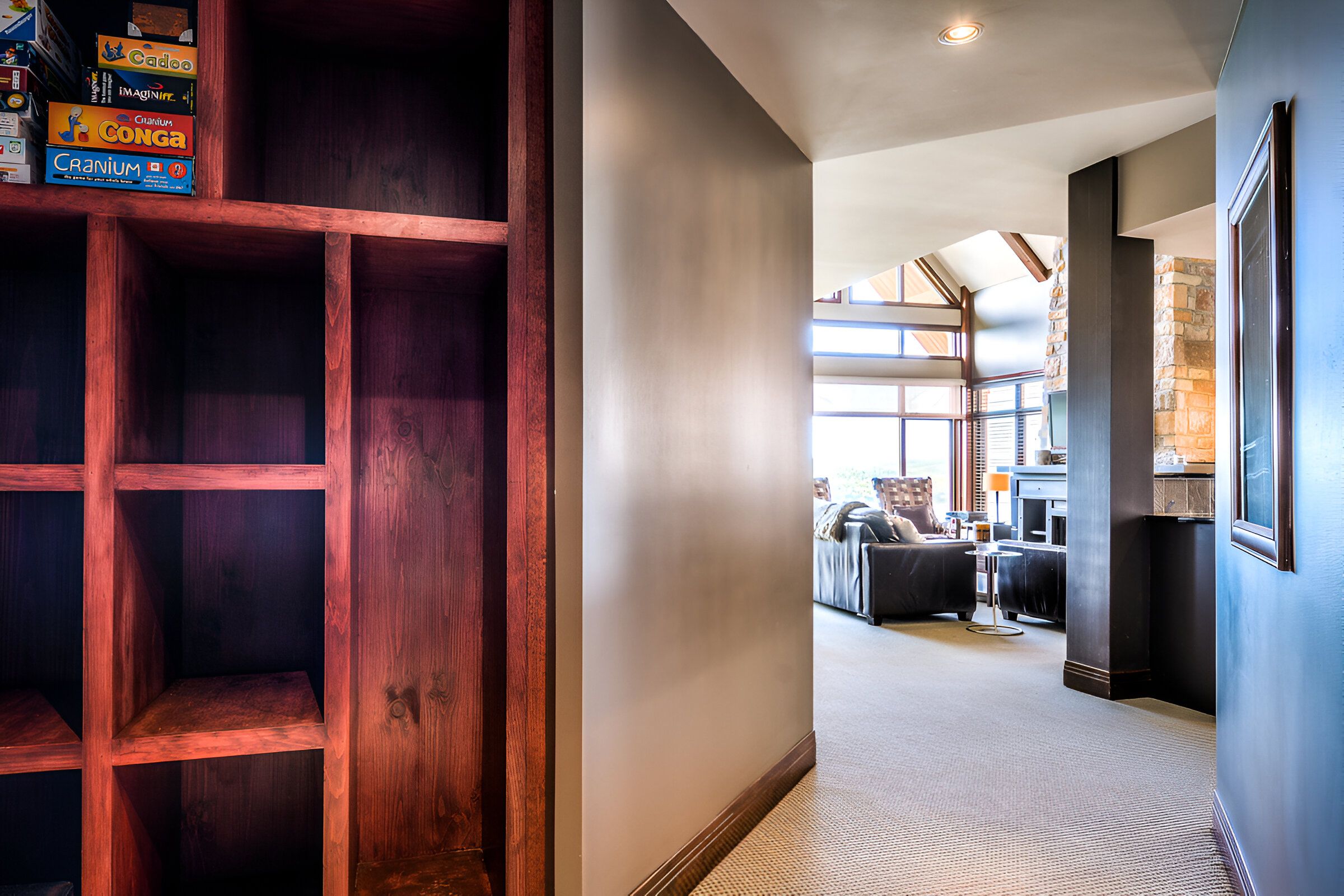 Un pasillo con una estantería de madera, una sala de estar moderna con sofás y una pared de acento de piedra.