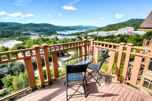 A balcony with a glass table and chair, overlooking a town and hills. - Altitude - Tremblant Luxurious Ski-in Ski-out Condo - Breathtaking Views (Mont-Tremblant)