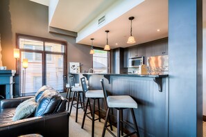A modern kitchen with bar stools, a microwave, and a refrigerator. - Altitude - Tremblant Luxurious Ski-in Ski-out Condo - Breathtaking Views (Mont-Tremblant)