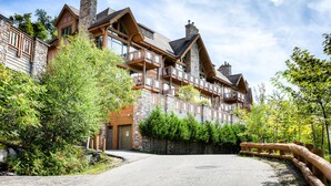 A multi-story lodge with a stone facade, wooden balconies, and a gravel driveway. - Altitude - Tremblant Luxurious Ski-in Ski-out Condo - Breathtaking Views (Mont-Tremblant)