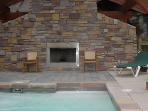 Ein Steinkamin mit zwei Holzstühlen, einem Pool und einer Liege.