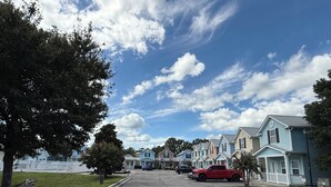 A residential street with houses, parked cars, and a clear sky.