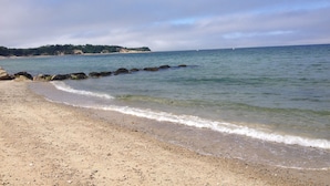 Una playa con agua cristalina, piedras y un área boscosa al fondo.
