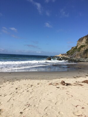A sandy beach with waves crashing onto rocks and a clear blue sky.