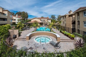 A hotel courtyard with a swimming pool, lounge chairs, and a hot tub.