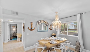 A dining area with a wooden table, white chairs, a chandelier, and nautical decor.