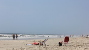 Una playa con gente, una silla roja y una tumbona azul.