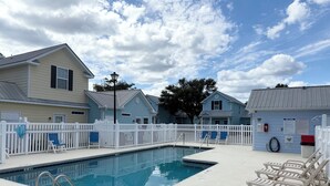 Una piscina con recinzione bianca, lettini da relax e una postazione per il bagnino.