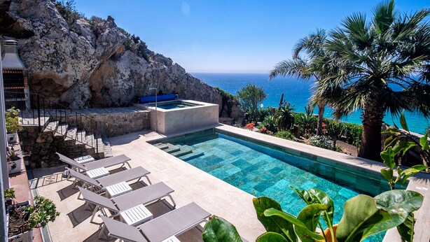 Área da piscina com espreguiçadeiras, uma banheira de hidromassagem e vista para o oceano.