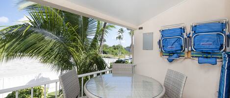 Een balkon met een glazen tafel en rieten stoelen, met uitzicht op water en palmbomen.