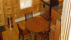 Ein Holzhütten-Innenraum mit Esstisch, Stühlen, einem Kühlschrank und einer Pendelleuchte.