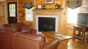 Ein gemütliches Blockhaus-Interieur mit Ledersofa, Kamin und Fernseher auf einem Holzständer.