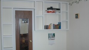 A hallway with a wooden door, a mirror, and a white wall with a calendar and bookshelves.