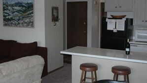 A compact living space with a kitchenette, a dining area with stools, a couch, and a painting on the wall.