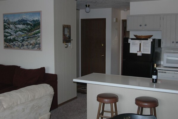 A compact living space with a kitchenette, a dining area with stools, a couch, and a painting on the wall.