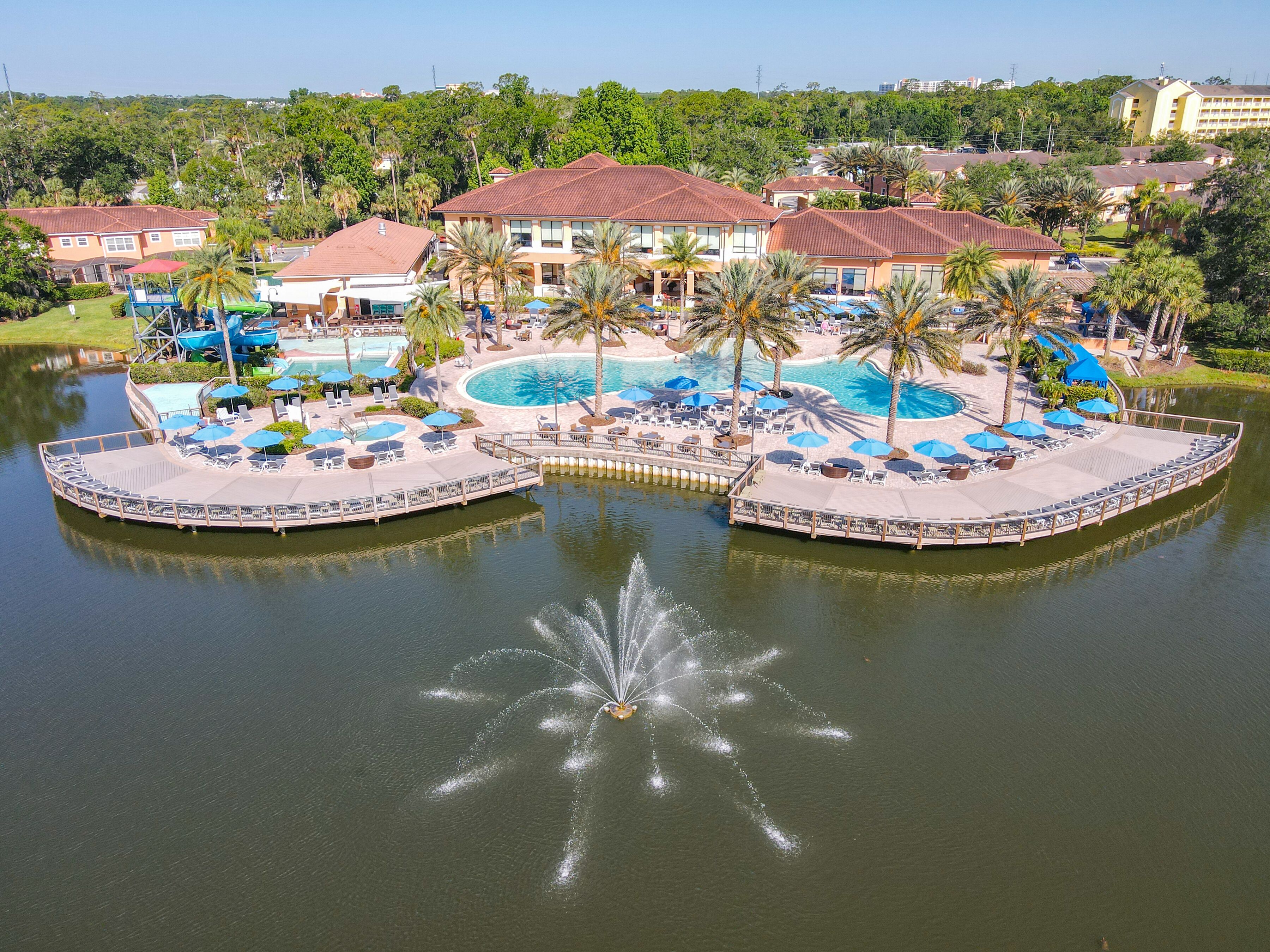 Un resort con piscina central, palmeras y una fuente de agua.