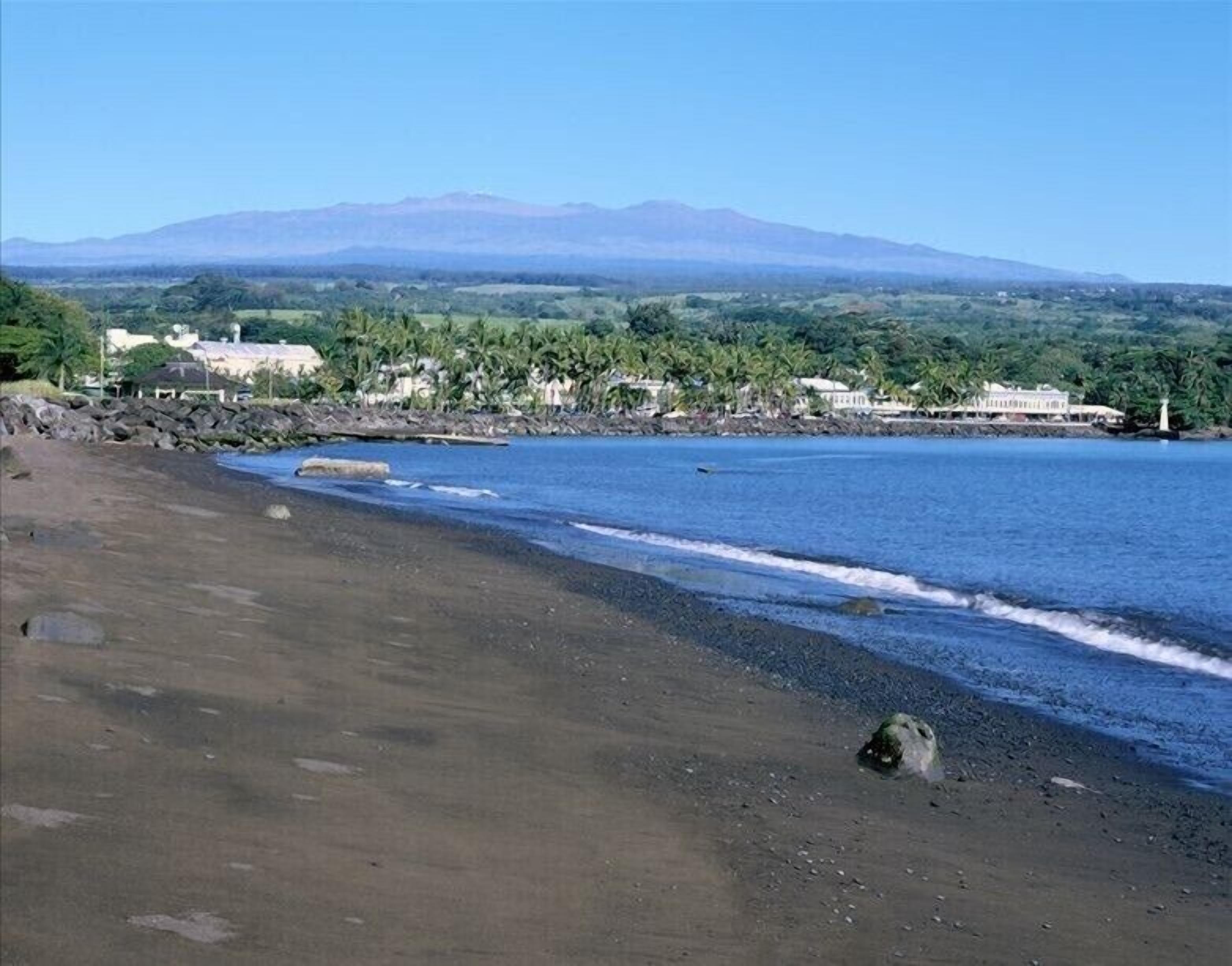 A beach with a mountain in the background, clear skies, and a calm sea.