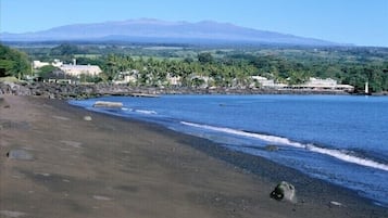 A beach with a mountain in the background, clear skies, and a calm sea.