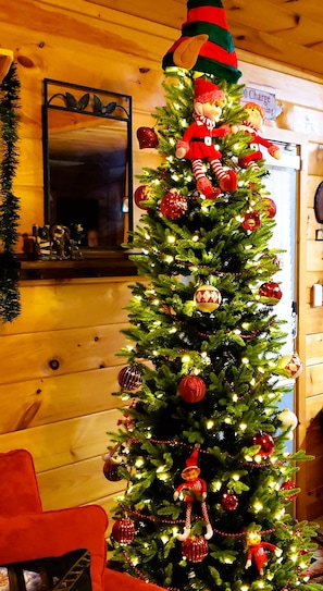 Un sapin de Noël décoré d’ornements et surmonté d’un casse-noisette, placé devant un mur en bois orné d’un miroir et d’une enseigne.