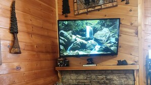 A cozy cabin interior with a stone fireplace, a red sofa, a television mounted above the fireplace, and wooden walls. - Private Hideaway near Pigeon Forge; Convenient to Attractions; Five-Star Reviews (Sevierville)