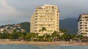 A beachfront hotel with multiple floors, palm trees, and a beach in the foreground. - Beachfront Panoramic Oceanview Modern Luxury (Old Town Romantic Zone) (Puerto Vallarta)