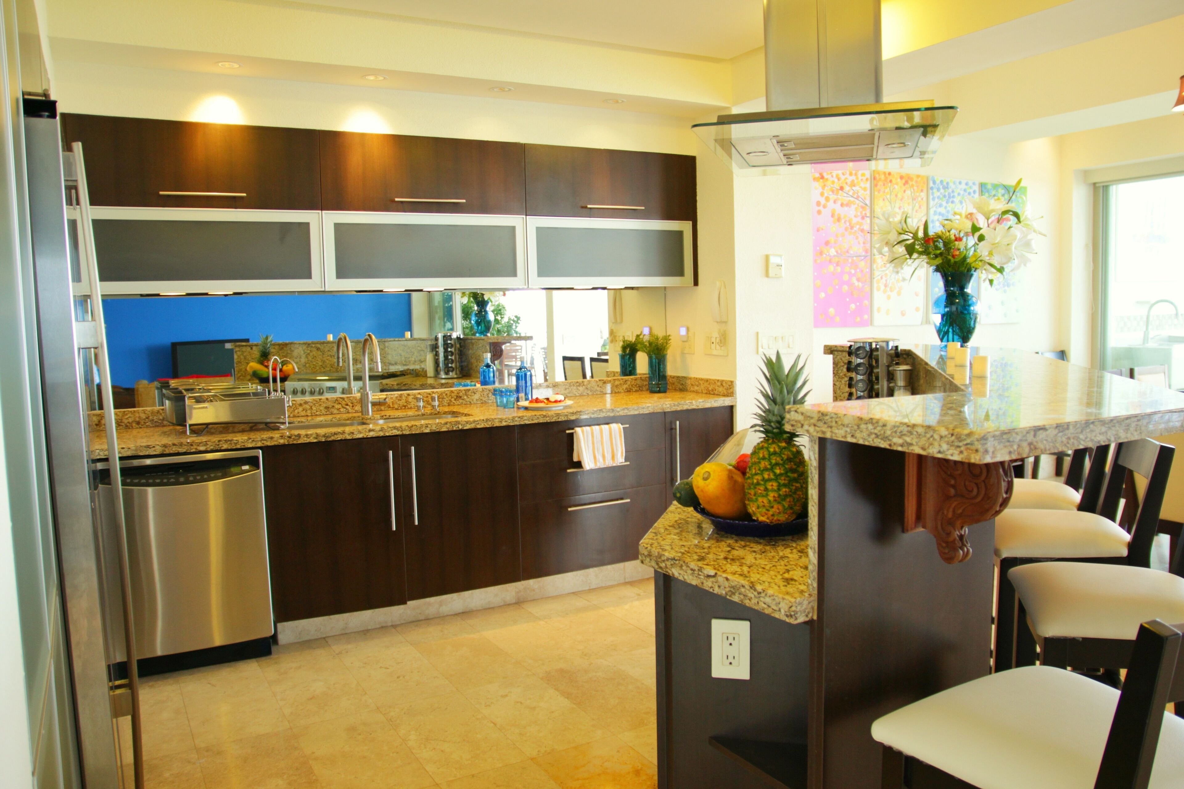 Cocina moderna con armarios oscuros, encimeras de granito, electrodomésticos de acero inoxidable y una isla central con frutero.