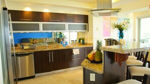 A modern kitchen with dark cabinetry, granite countertops, stainless steel appliances, and a central island with a fruit bowl. - Beachfront Panoramic Oceanview Modern Luxury (Old Town Romantic Zone) (Puerto Vallarta)