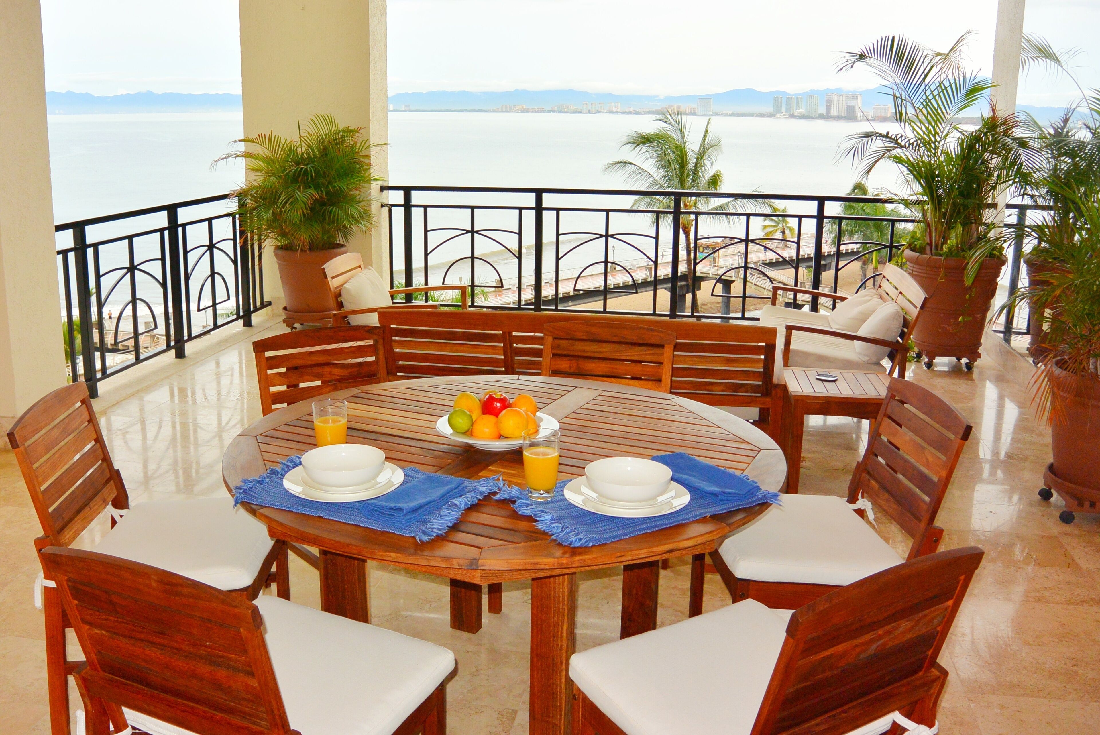 A round wooden dining table with white chairs, a fruit bowl, and a glass of orange juice.