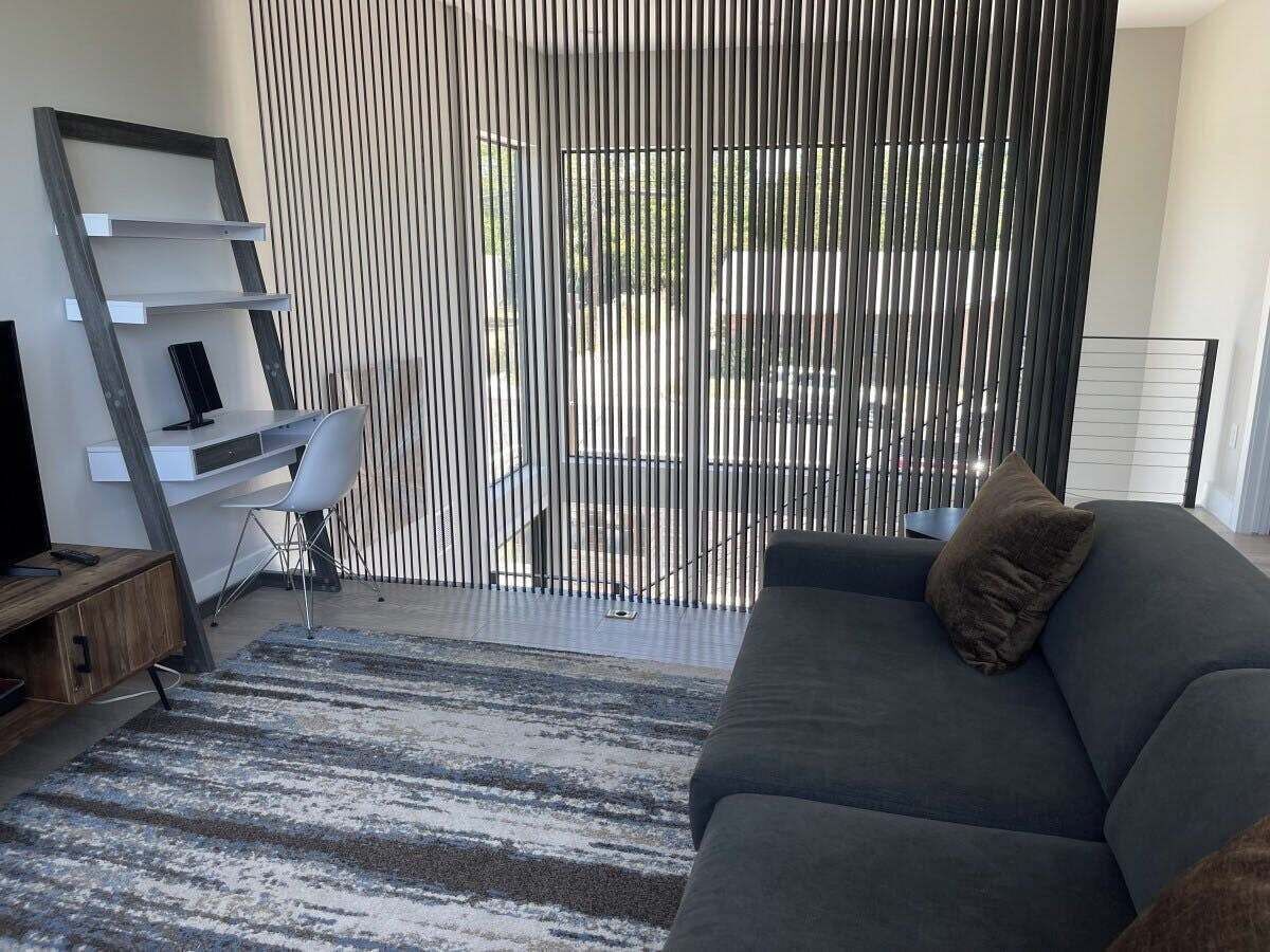 Een moderne woonkamer met een grijze bank, een houten kast, een witte stoel en een gestreept vloerkleed.