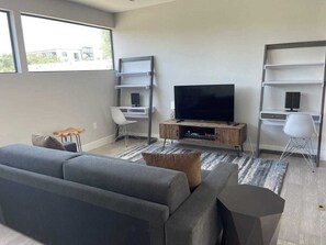 A modern living room with a sofa, TV, and built-in shelves. - Modern 5BR Oasis | 2-Home w/ Pool & Hot Tub (Austin)