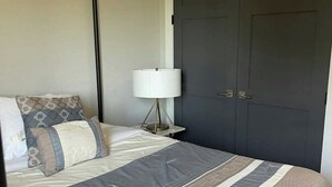 Ein Schlafzimmer mit einem Bett, einem Nachttisch, einer Lampe und einem dunkelbraunen Kleiderschrank.