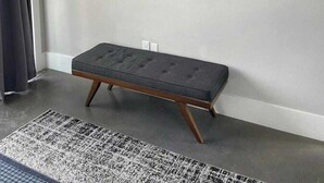 Ein modernes Wohnzimmer mit einem an der Wand montierten Flachbildfernseher, einer dunkelgrauen Bank und einem gemusterten Teppich auf dem Boden.