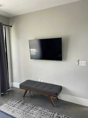 Ein modernes Wohnzimmer mit einem an der Wand montierten Flachbildfernseher, einer dunkelgrauen Bank und einem gemusterten Teppich auf dem Boden.