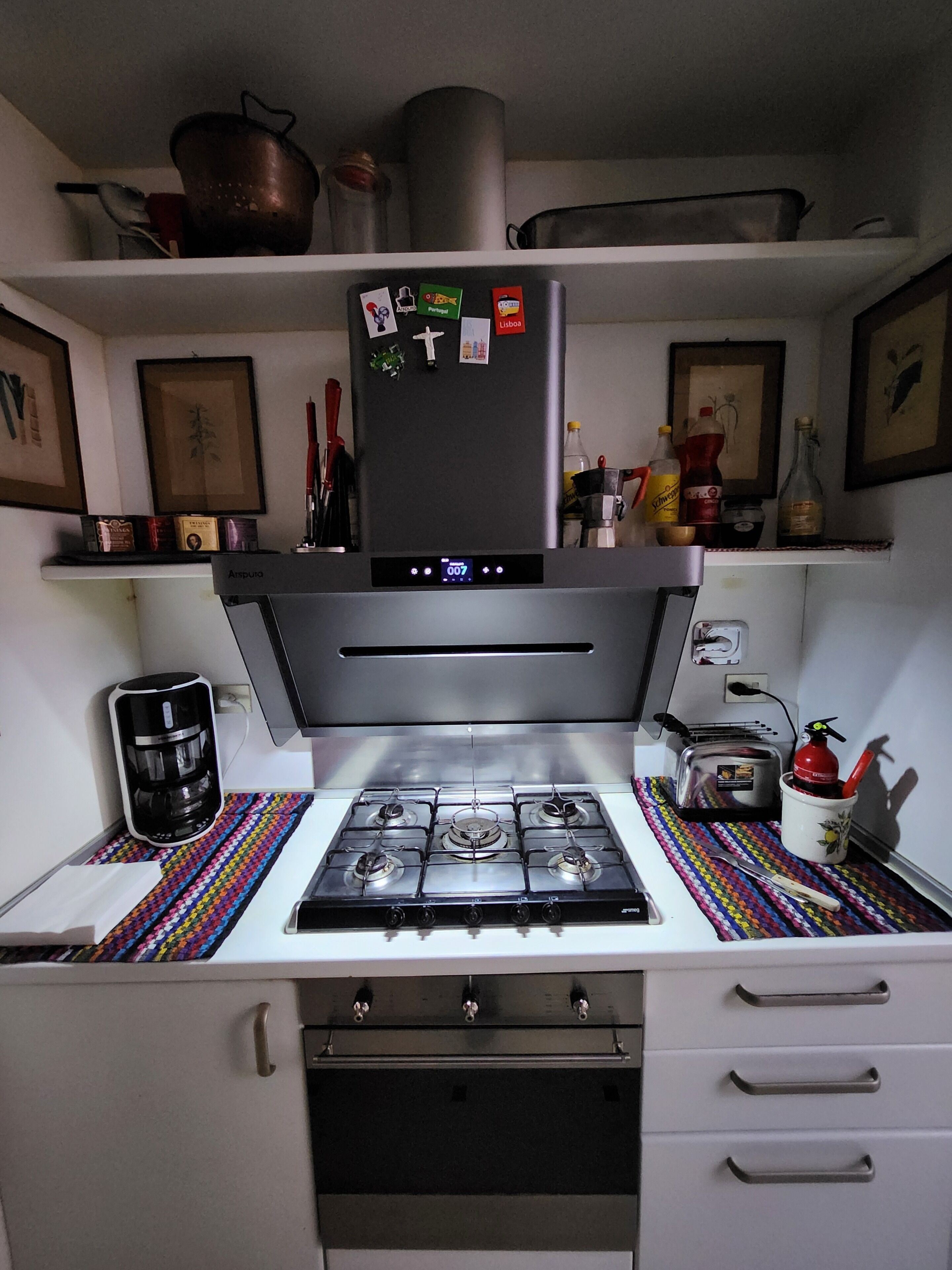 Une cuisine de taille réduite équipée d’une cuisinière à gaz, d’une machine à café et d’un réfrigérateur.