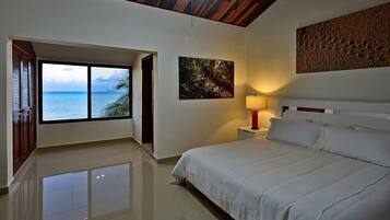 A bedroom with a large window, a bed, a nightstand, and a wall-mounted artwork.