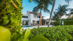 Une maison moderne avec une piscine, entourée d’une végétation luxuriante et de palmiers.