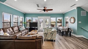 A living room with a brown leather sofa, a ceiling fan, a TV, and a dining area with a table and chairs. - Waterfront luxury! Free bikes & kayaks! Great fishing! Bike to the beach! (Galveston)