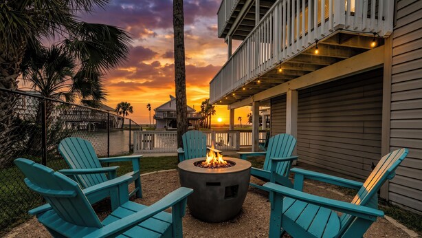 A patio with a fire pit, outdoor seating, and a view of the sunset. - Waterfront luxury! Free bikes & kayaks! Great fishing! Bike to the beach! (Galveston)